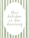 A square decorative print or card featuring the phrase 'this kitchen is for dancing' in light sage green script inside a large white oval, set against a background of vertical sage green and white brushstroke stripes.